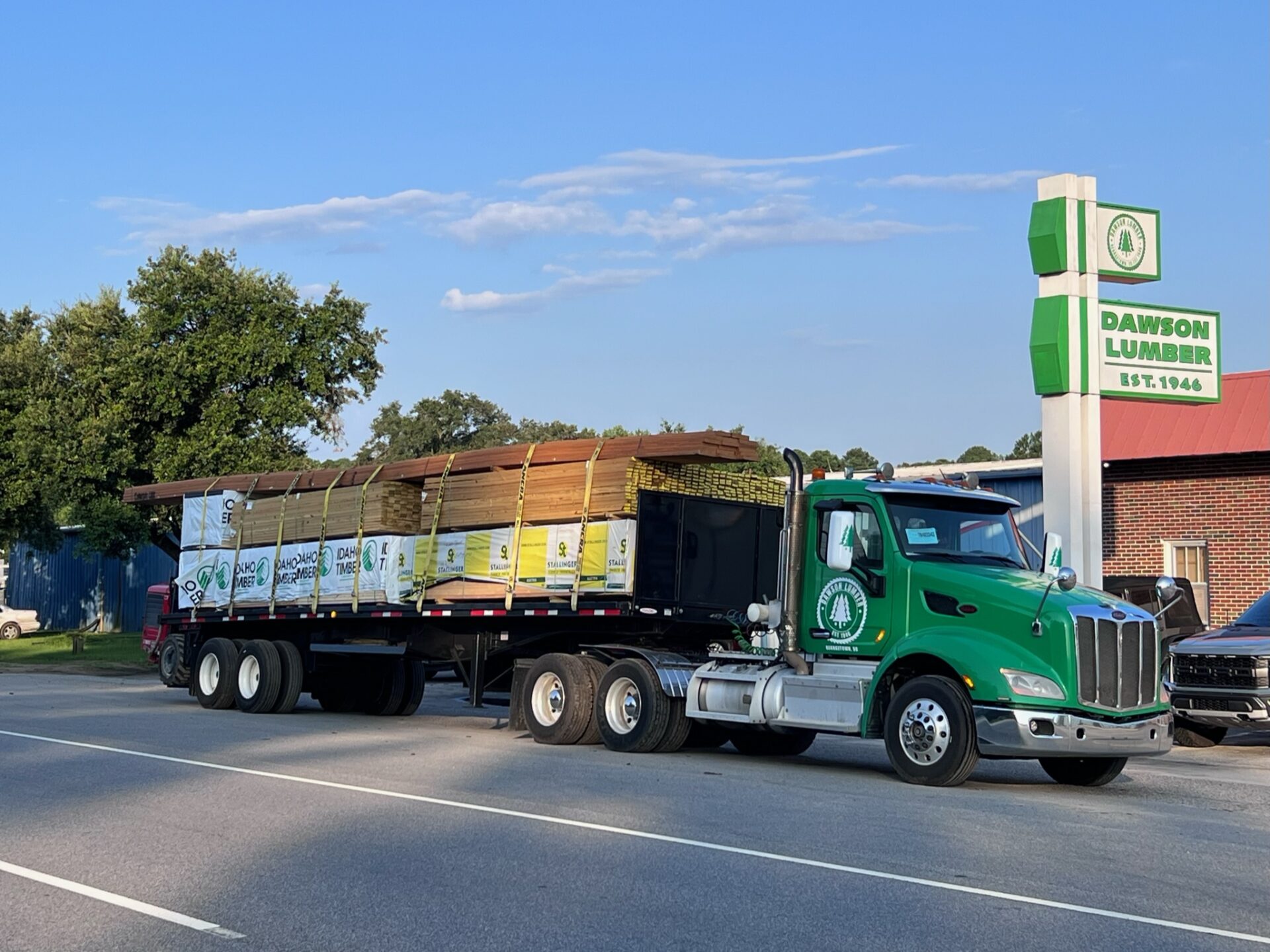 A green semi truck with a trailer on the road.